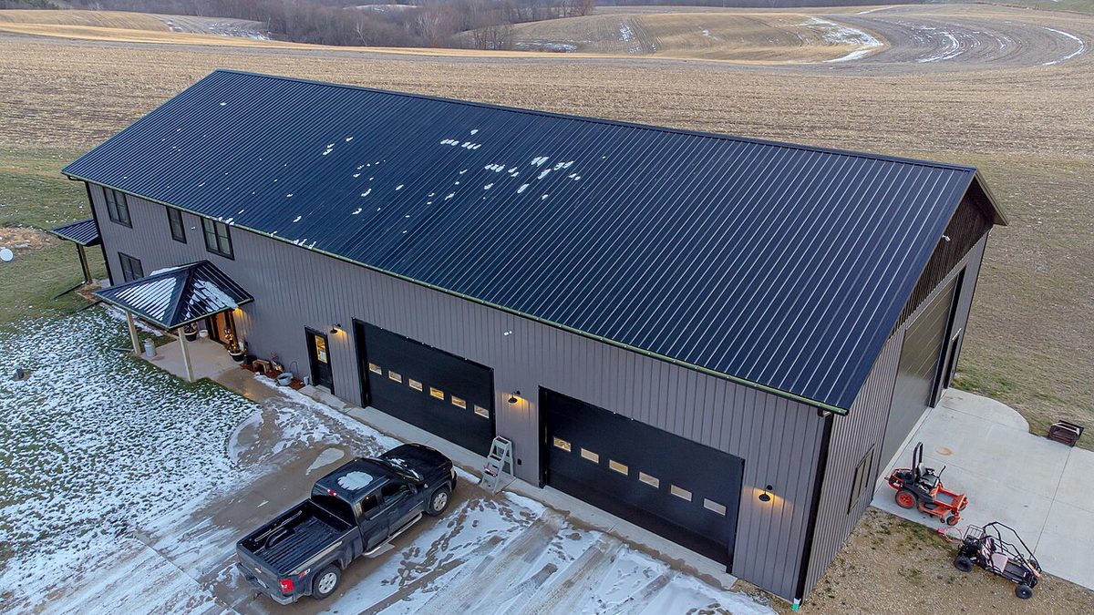 Charcoal metal barndominium with living windows, porch, and large shop doors on acreage.